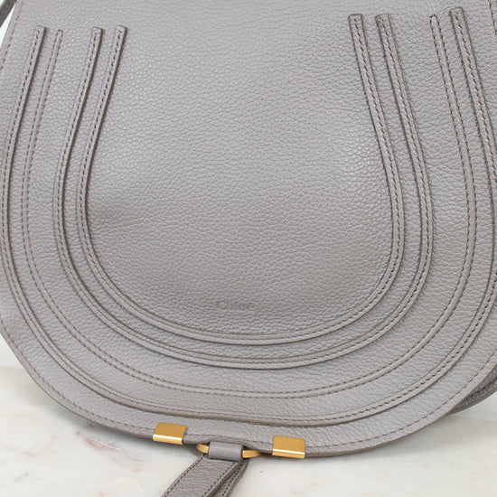 A light gray pebbled leather shoulder bag with gold-tone hardware, shown on a white marble surface.