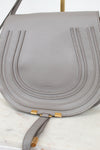 A light gray pebbled leather shoulder bag with gold-tone hardware, shown on a white marble surface.