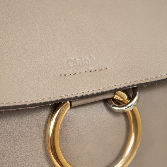 Close-up of a taupe leather handbag with a gold-tone O-ring handle and an embossed Chloé logo on the flap.