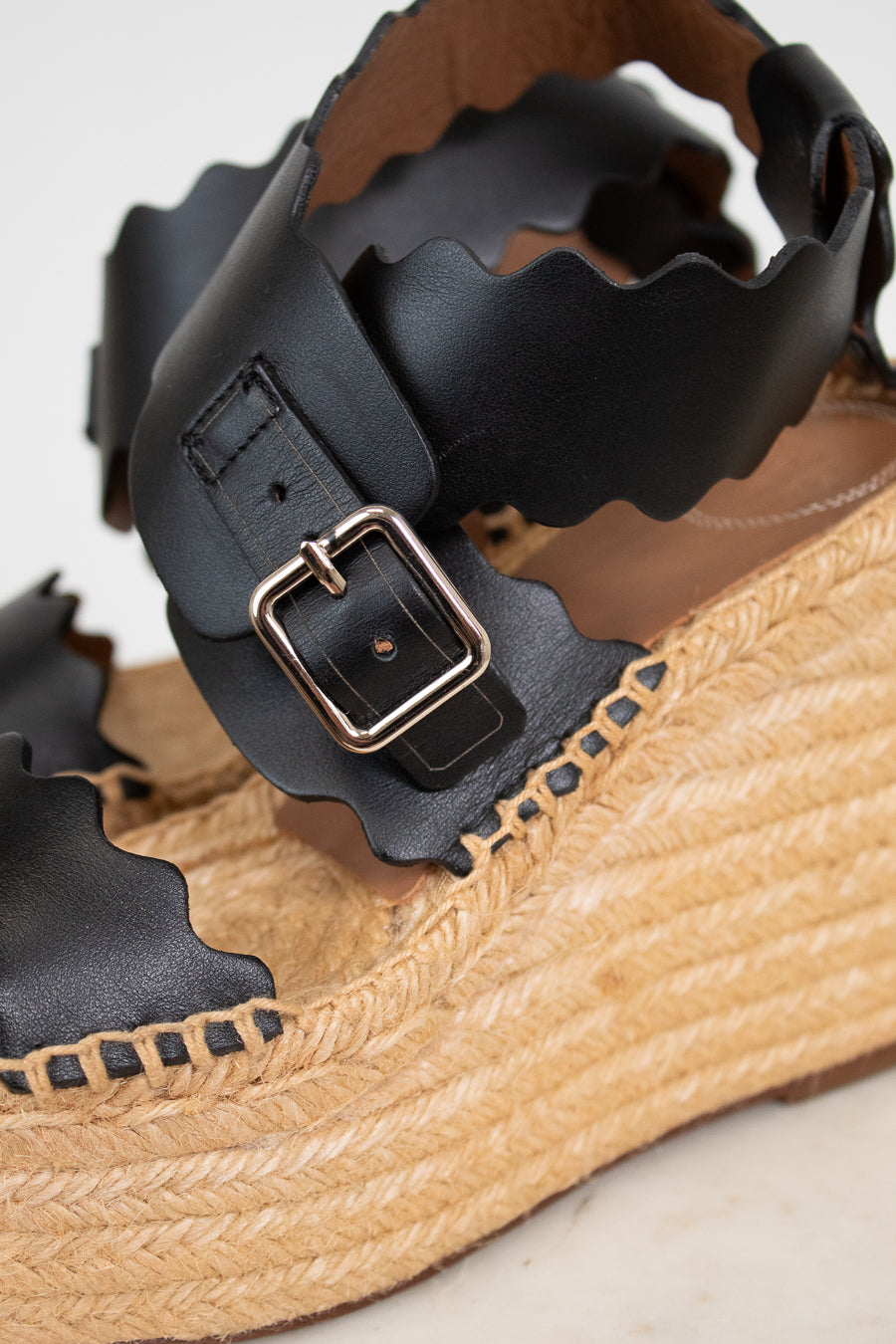 Close-up of a sandal with black leather straps and a tan woven sole.