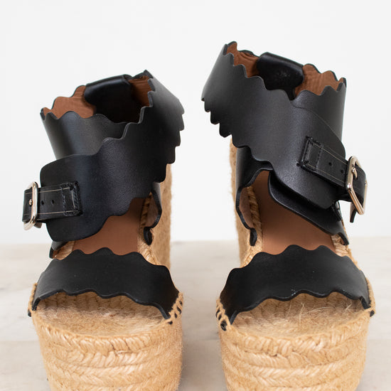 Black wedge sandals with wicker soles on a white background