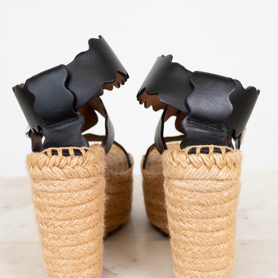 Pair of wedge sandals with black straps and woven beige sole on a light background