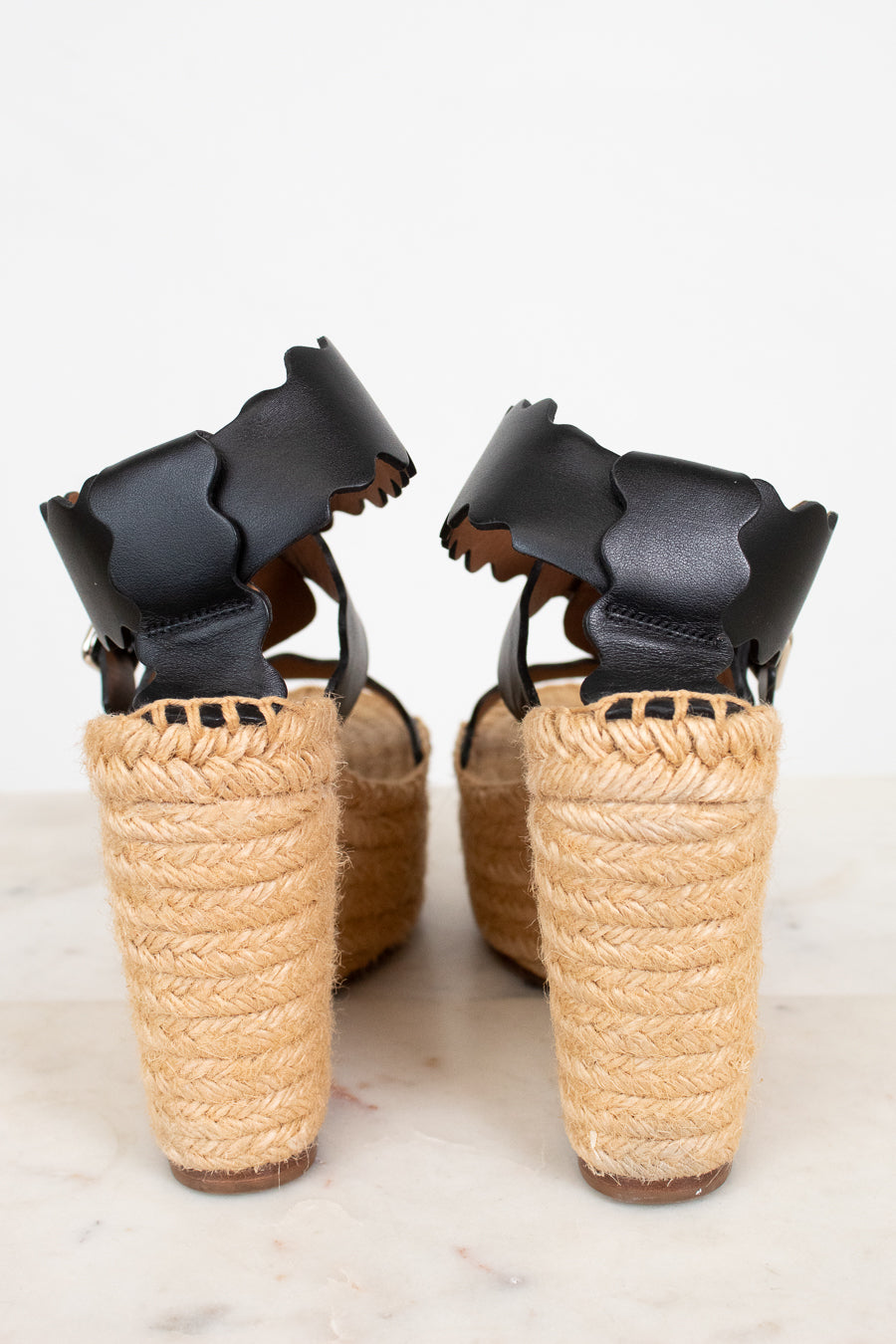 Pair of wedge sandals with black straps and woven beige sole on a light background