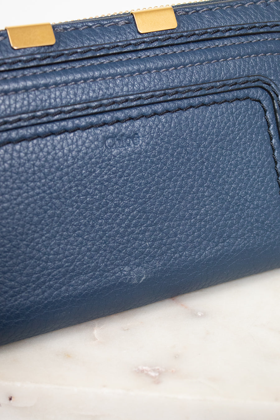 Close-up of a blue textured wallet with gold accents on a marble surface