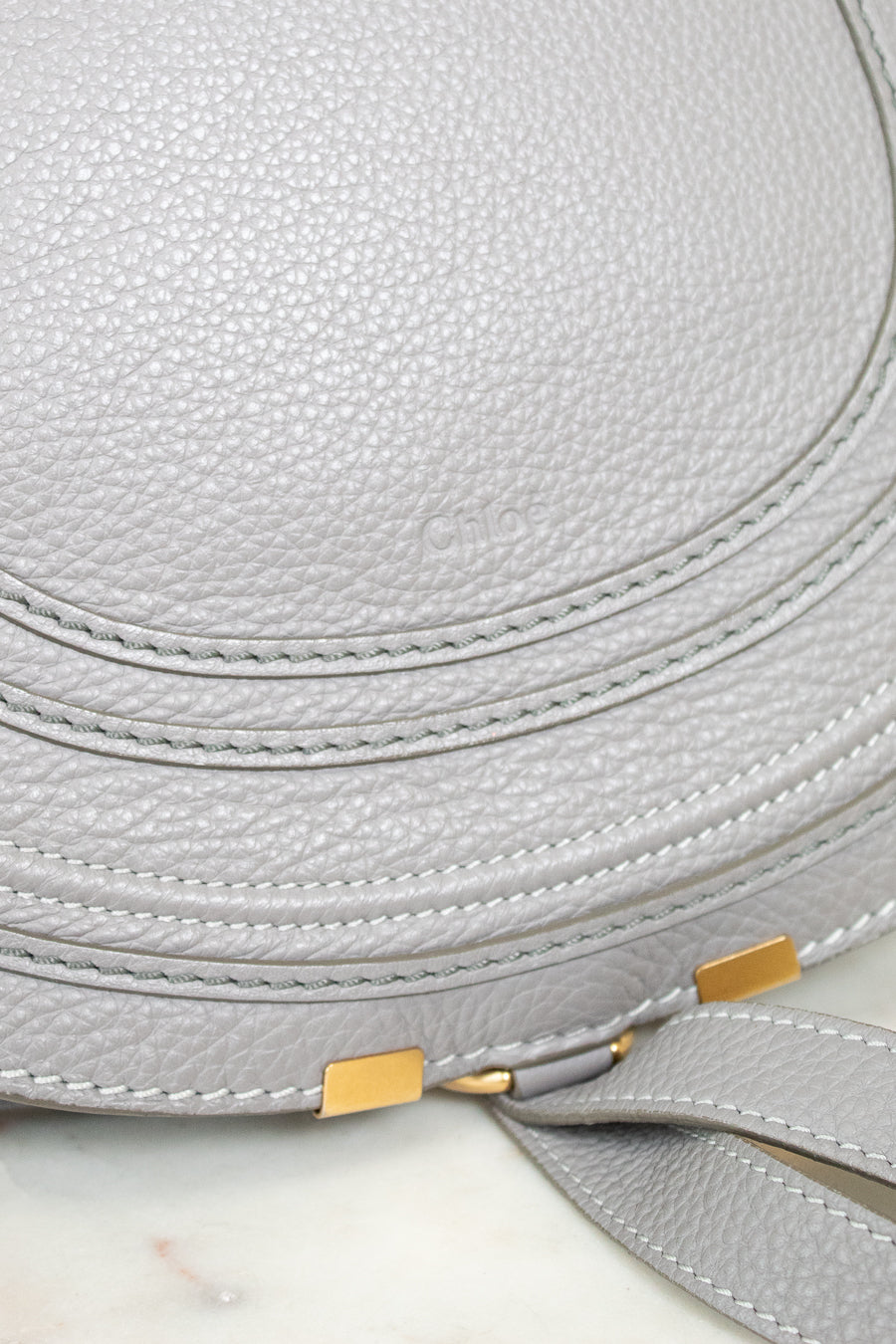 Close up of grey leather saddle crossbody bag with hold hardware on white background