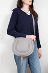 Person wearing navy sweater and jeans holding a grey saddle crossbody bag on a white background