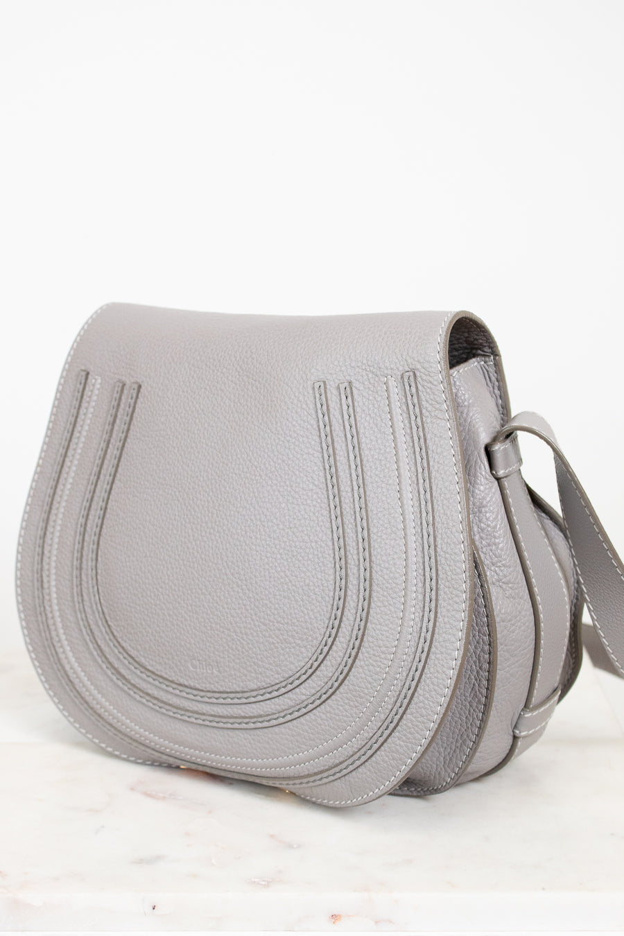 Grey leather saddle crossbody bag on white background