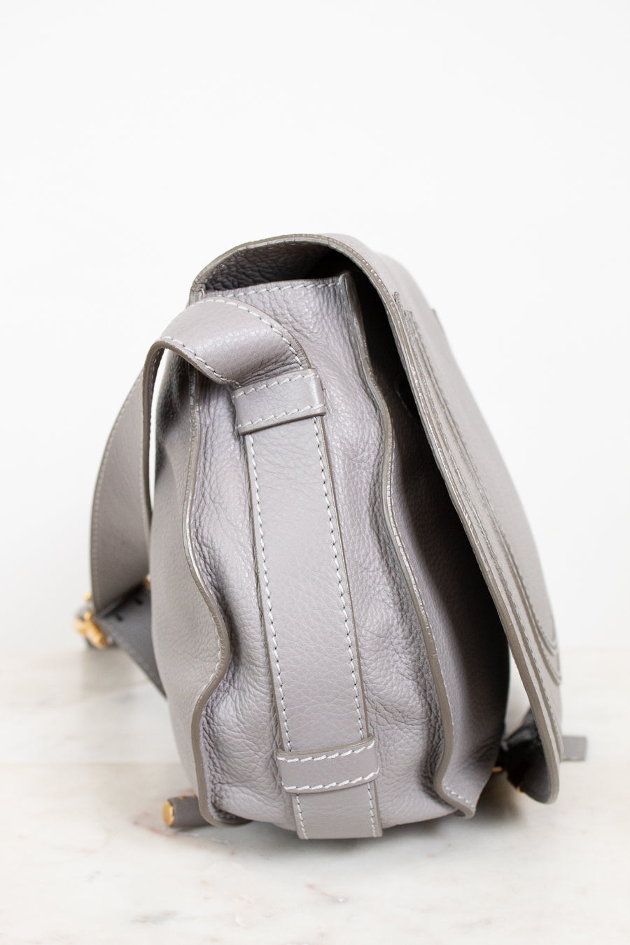 Side view of grey leather saddle crossbody bag on white background