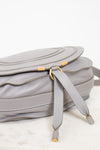 Bottom view of grey leather saddle crossbody bag with gold hardware on white background