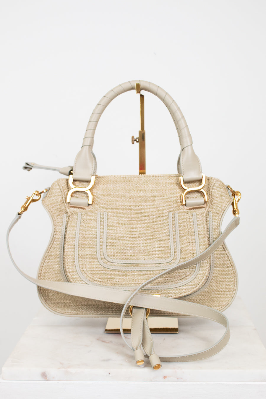 Beige handbag with straw texture and gold accents on a white background