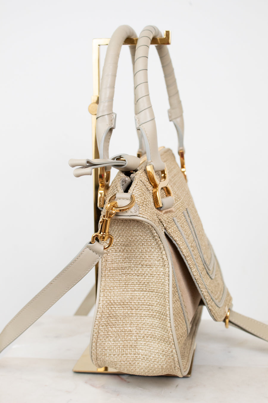 Beige handbag with straw texture and gold accents on a white background