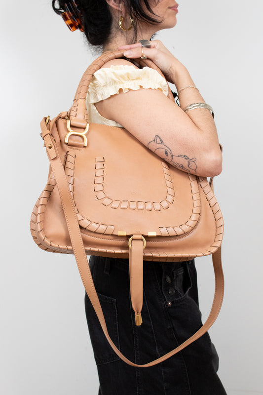 Person holding a tan leather handbag against a plain background