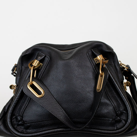 Black leather handbag with gold hardware on a white background
