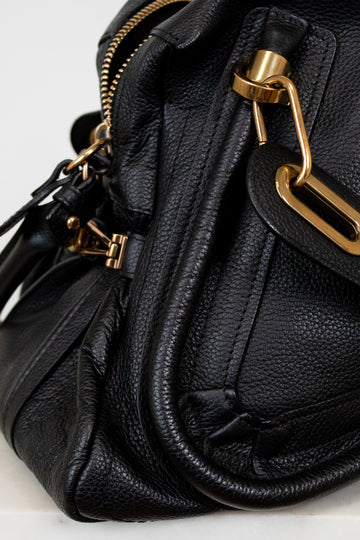 Black leather handbag with gold hardware on a light gray background