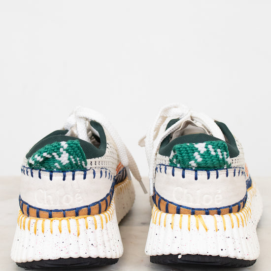Pair of white sneakers with green and blue accents on a light background