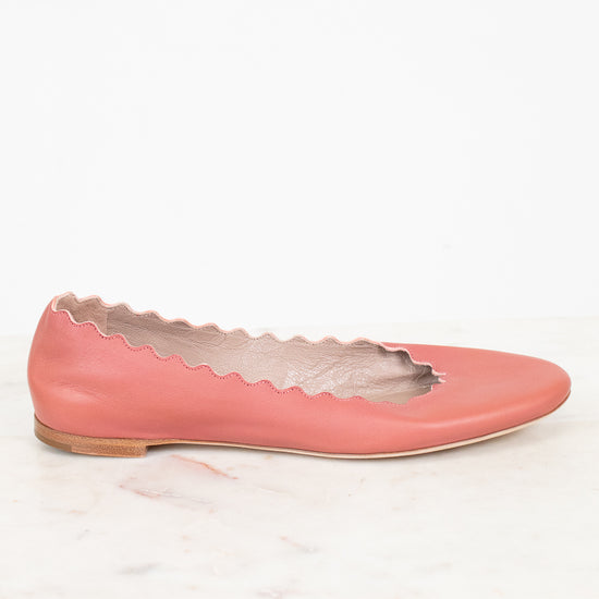A single dusty pink leather flat shoe with a scalloped cutout edge detail, resting on a white marble surface against a white background.