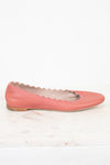 A single dusty pink leather flat shoe with a scalloped cutout edge detail, resting on a white marble surface against a white background.