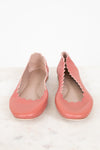 A pair of dusty pink leather ballet flats with scalloped edges, shown from the side on a light marble surface against a white background.