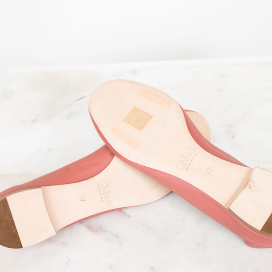 A pair of pink leather ballet flats shown from the bottom, displaying the light beige insole and heel counter, resting on a white marble surface.