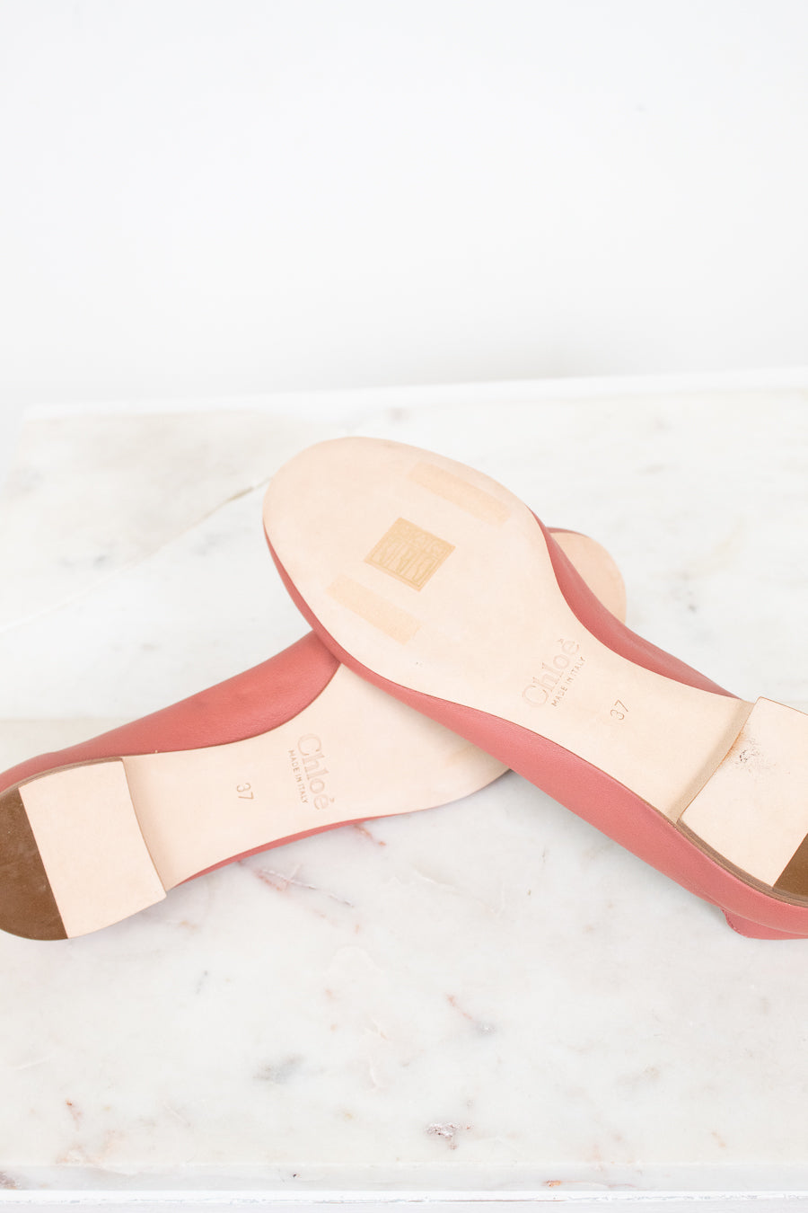 A pair of pink leather ballet flats shown from the bottom, displaying the light beige insole and heel counter, resting on a white marble surface.