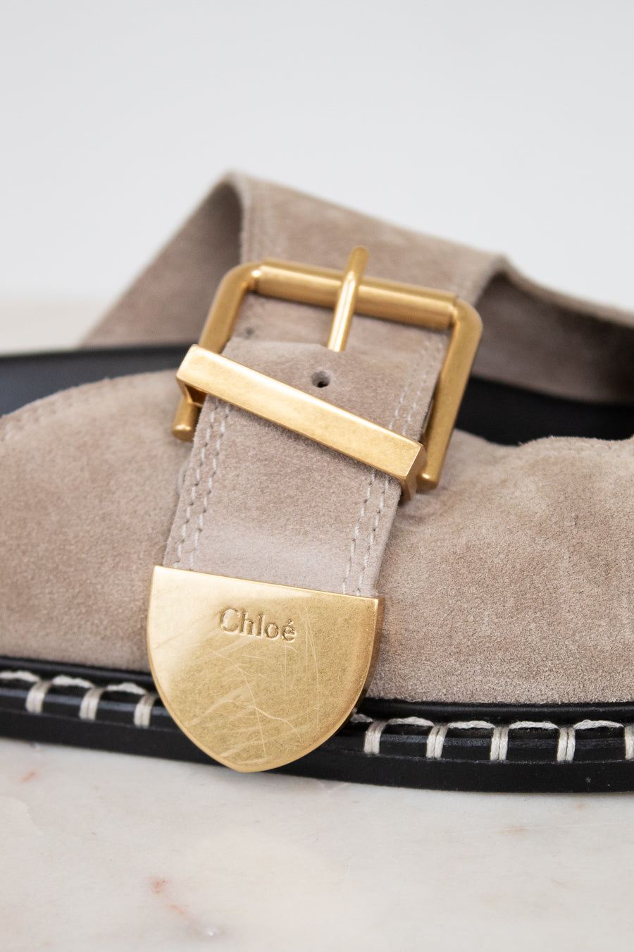 Close-up of a sandal with a gold buckle and 'Chloe' logo on a light background
