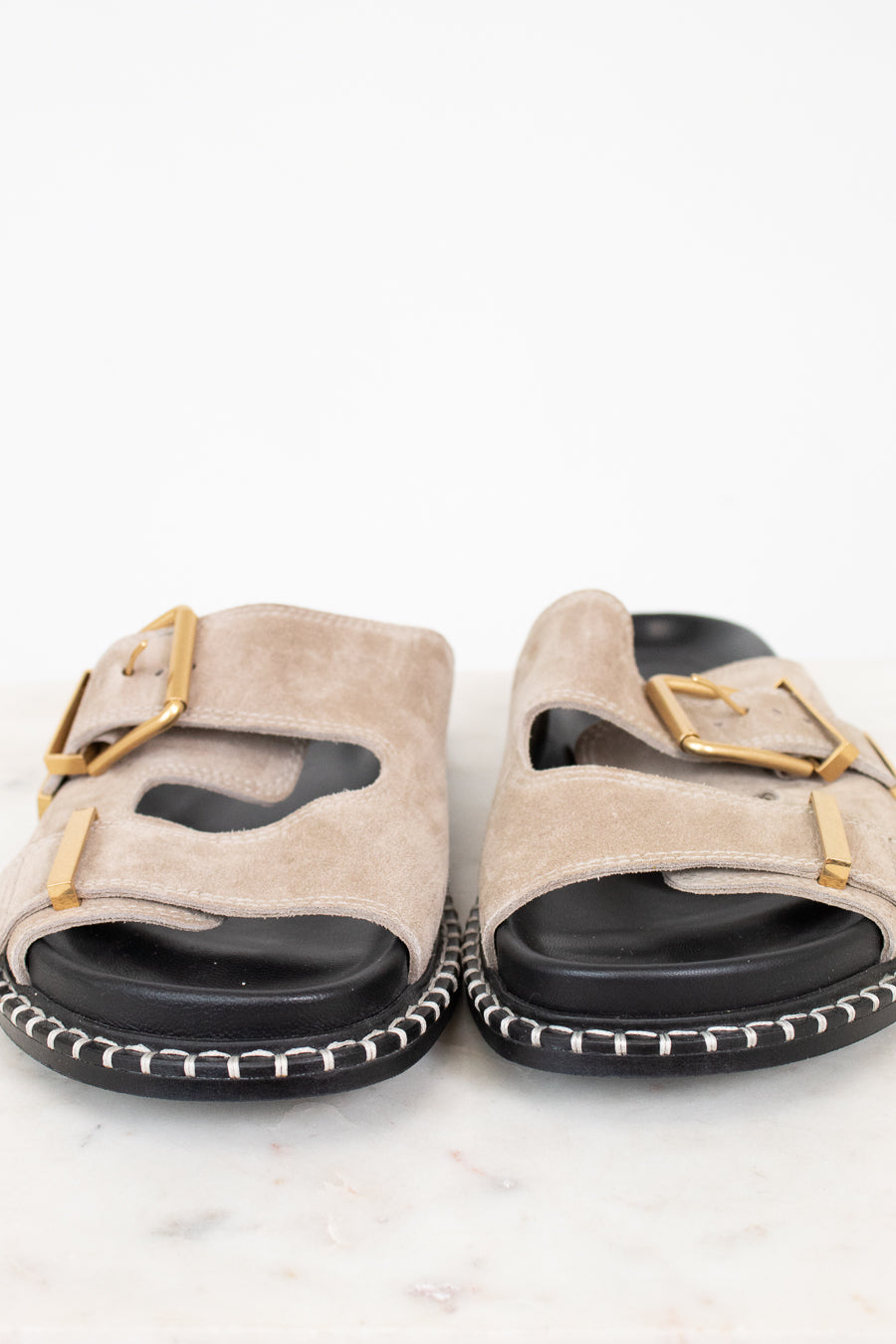 Pair of beige sandals with gold buckles on a white background
