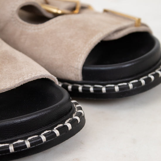 Pair of beige sandals with black soles on a light background