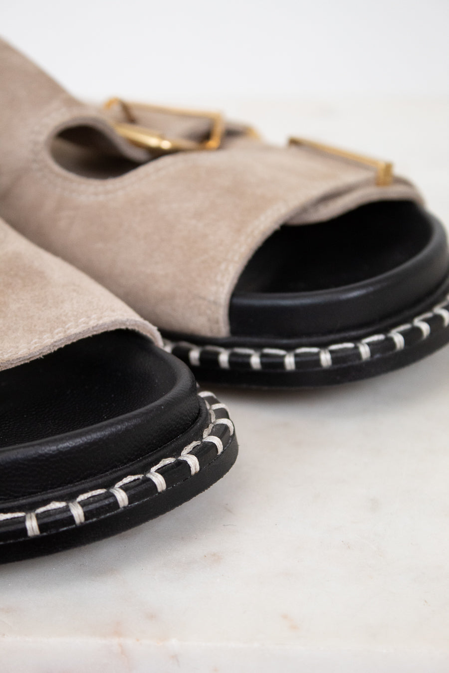 Pair of beige sandals with black soles on a light background