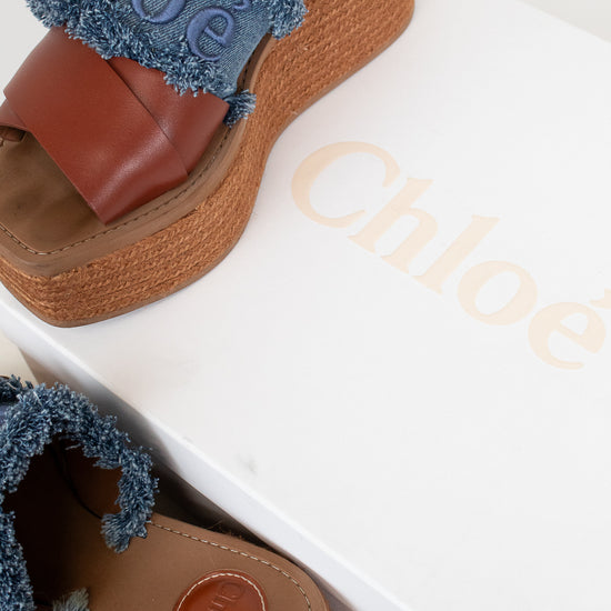 A pair of Chloé wedge sandals with brown leather straps, blue frayed trim, and jute platform espadrille soles, shown with a white Chloé shoebox.