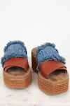 A pair of platform slide sandals featuring blue denim straps with frayed edges, embossed 'Chloé' lettering, and a brown leather strap, set on a woven jute platform sole.