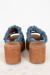 A pair of women's espadrille wedge sandals with frayed blue denim-style straps and brown woven jute platform soles, shown from the back on a light marble surface.