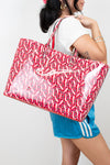 Person holding a large red and white patterned tote bag against a plain background