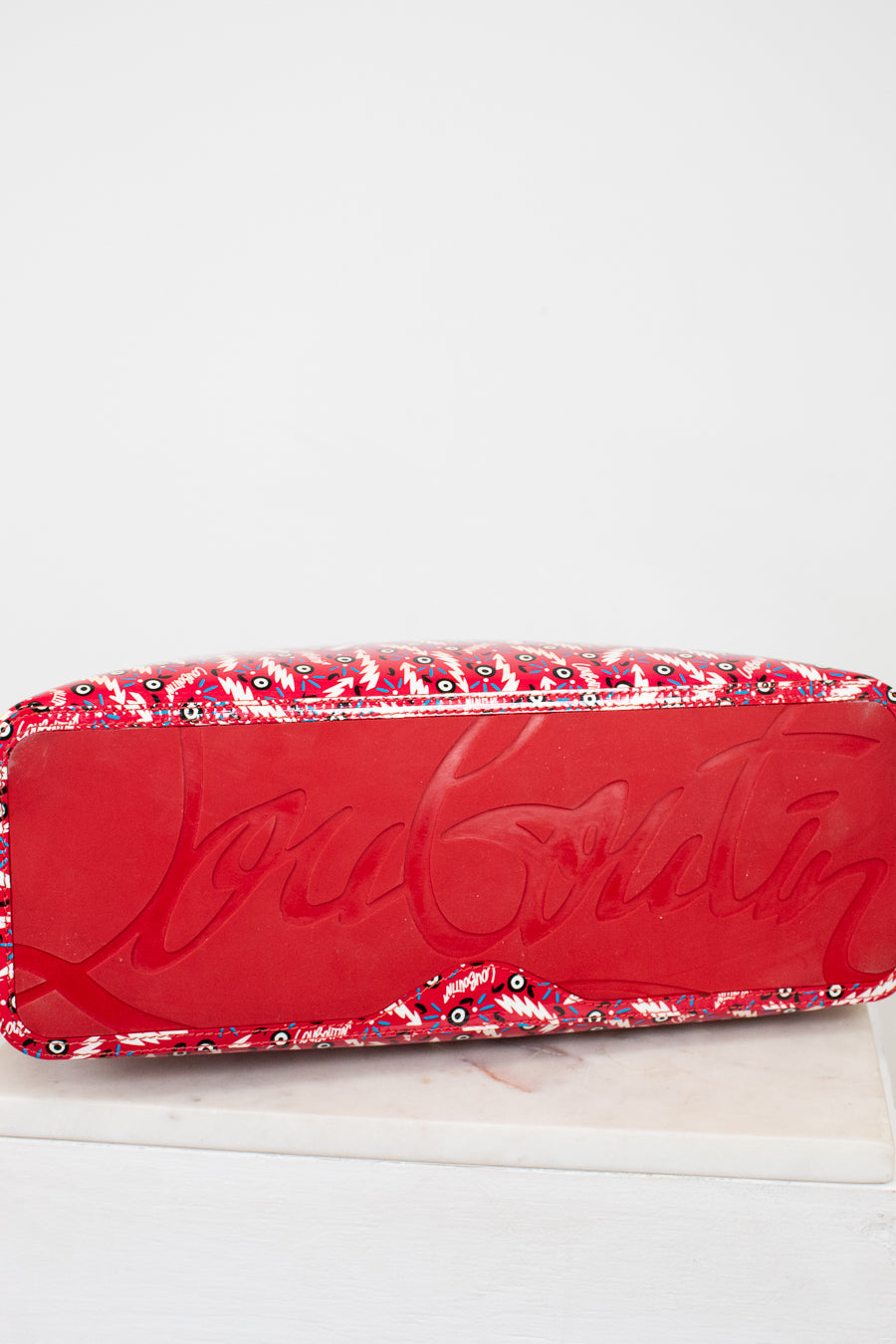Red base of Louboutin tote with abstract pattern on a white background
