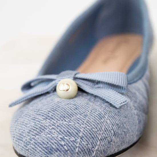 Blue flat shoe with a bow and pearl detail on a light background