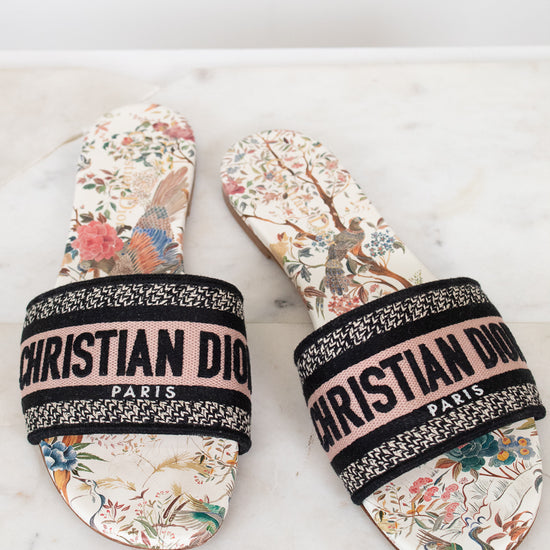 Pair of floral sandals with 'Christian Dior' woven into black/white/pink strap on a marble surface and white background