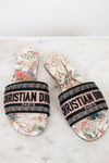 Pair of floral sandals with 'Christian Dior' woven into black/white/pink strap on a marble surface and white background