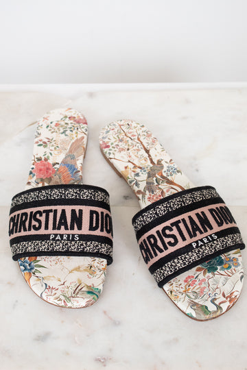 Pair of floral sandals with 'Christian Dior' woven into black/white/pink strap on a marble surface and white background