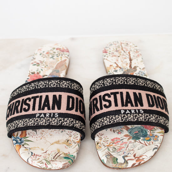 Pair of floral sandals with 'Christian Dior' woven into black/white/pink strap on a marble surface and white background