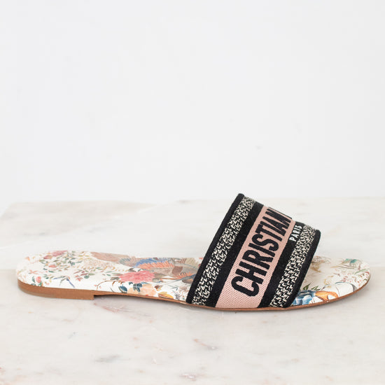 Side view of floral sandals with 'Christian Dior' woven into black/white/pink strap on a marble surface and white background