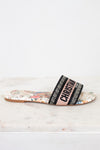 Side view of floral sandals with 'Christian Dior' woven into black/white/pink strap on a marble surface and white background