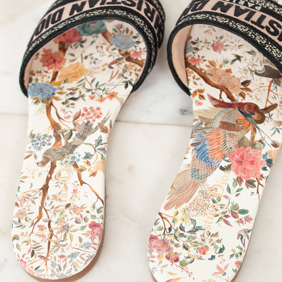 Floral sandals with 'Christian Dior' woven into black/white/pink strap on a marble surface and white background