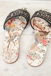 Floral sandals with 'Christian Dior' woven into black/white/pink strap on a marble surface and white background