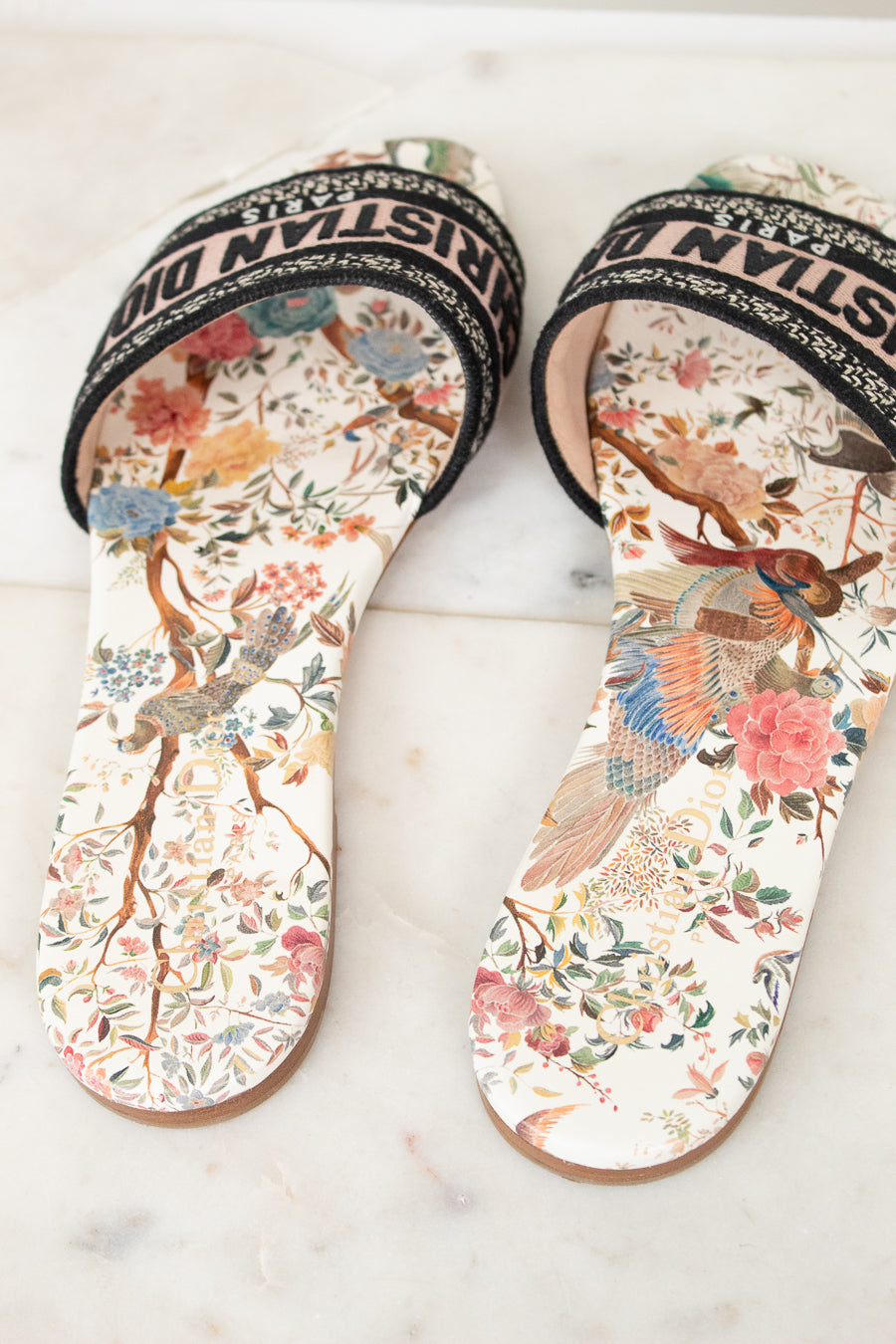 Floral sandals with 'Christian Dior' woven into black/white/pink strap on a marble surface and white background