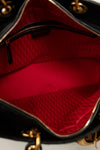 Close-up of the interior of a black handbag showing a bright red lined compartment with a gold-tone zipper and a repeating monogram pattern on the lining.
