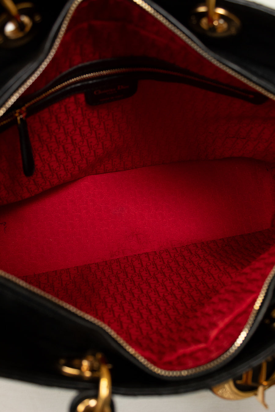 Close-up of the interior of a black handbag showing a bright red lined compartment with a gold-tone zipper and a repeating monogram pattern on the lining.