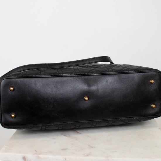 A black leather handbag shown from the bottom, featuring a quilted pattern, gold-tone feet, and a handle, resting on a white marble surface against a white background.