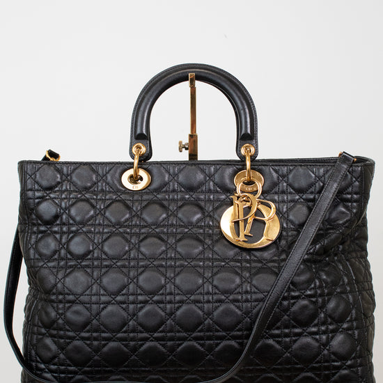 A black quilted leather top-handle handbag with gold-tone hardware, displayed on a white pedestal against a light gray background.