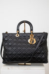 A black quilted leather top-handle handbag with gold-tone hardware, displayed on a white pedestal against a light gray background.
