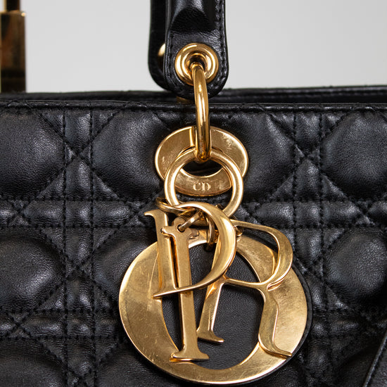 Close-up of a black quilted leather handbag with a large gold-tone Christian Dior CD logo charm hanging from a black leather handle.