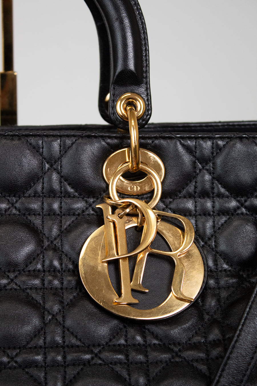 Close-up of a black quilted leather handbag with a large gold-tone Christian Dior CD logo charm hanging from a black leather handle.